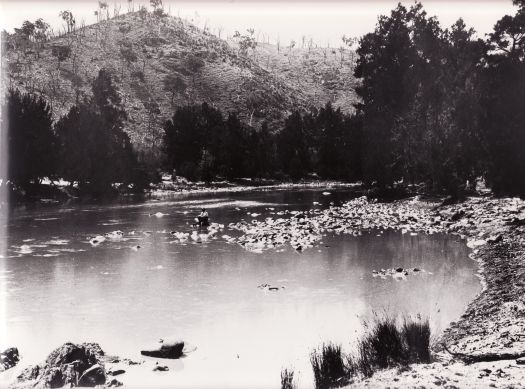 Cotter River area. A man is sitting on a rock, probably fishing in the middle of a river.