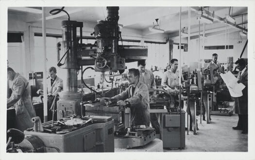 Internal shot of mechanical workshop, Mt Stromlo. Shows the machinery and seven men working.