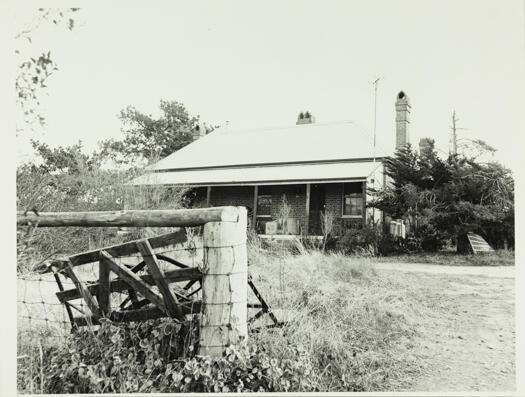 A front view of Tuggeranong schoolhouse. There is long grass in the yard.