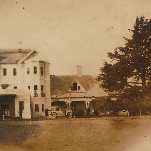 Rose Hunt's family photos. A view of Government House, Yarralumla with a car and driver parked near the front entrance. Five people are lined across the image.