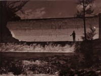 A photo of the Cotter Dam showing a man fishing in the pool below the dam wall.