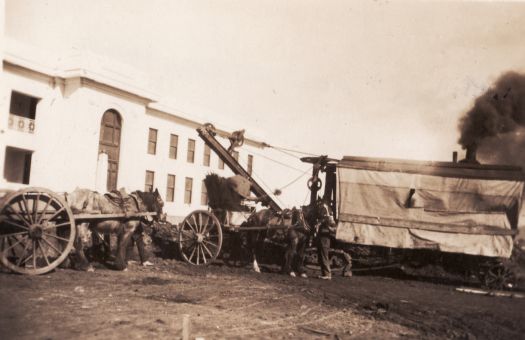 Horse and dray outfits and steam shovel in foreground of old Parliament House