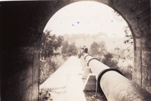 Two people sitting on the Cotter pipeline. Photo taken from a tunnel looking to the outside.