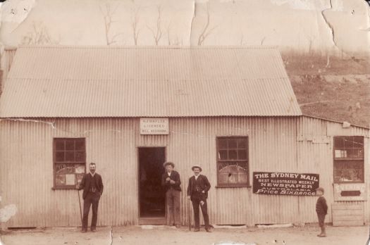 H J Naylor's Billiard Room, Captains Flat. Henry Naylor is standing on the left holding a billiard cue. Two other men and a boy are also standing. The building is made of corrugated iron.