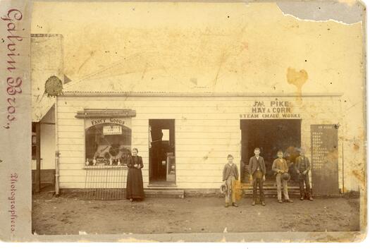 James Pike's hay and corn store, Crawford Street, Queanbeyan. Shows the front of the store in Crawford Street with four men and a woman in front.