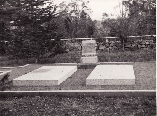 Graves of William and Nina Farrer at Lambrigg. A low stone wall and pine trees are behind the graves.