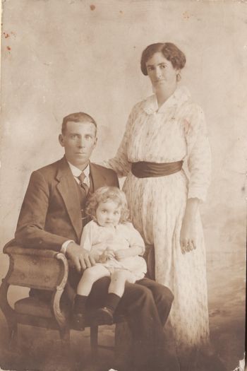 Parents and child. The mother is standing next to her seated husband who is holding their baby.  The wife 'Beat' was a niece of Mrs J. Wark of Gidleigh near Bungendore.