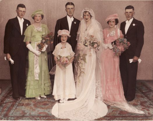 A coloured wedding photograph of Mr. and Mrs. Gordon Walker (nee C. Daniel)  showing the couple flanked on both sides by members of the bridal party and a flower girl in front.