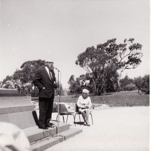 Commencement Stone ceremony on Capital Hill to mark Canberra Day in 1972. The ceremony was organised by the CDHS and shows the Society's president, Cam Morris, speaking and member Alma Wood seated. Eucalypts are in the background.