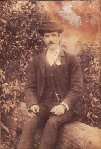 Young man in suit and hat sitting on a log.