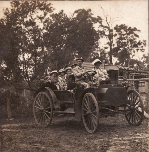 Thomas Nolan and family sitting in a car in front of their house at Glenwood. Nolan is in the front with his wife (who is nursing a baby). Four children sit in the back.