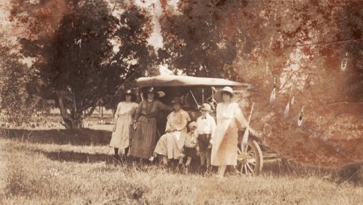Four women and two children in front of a car in a bushland setting.