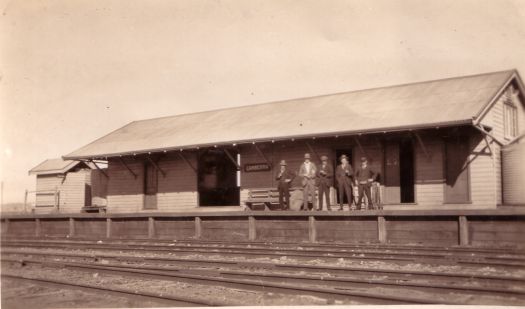 Canberra Railway Station showing four men and a porter, the railway lines and a weatherboard station building.