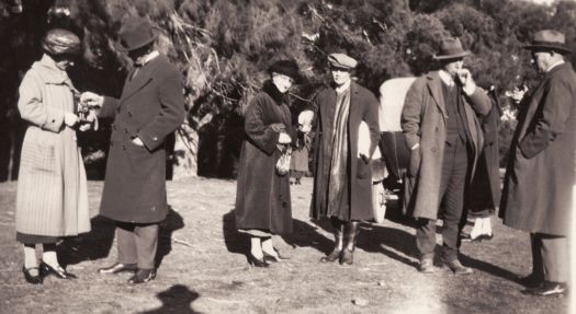 Unnamed visitors. A well dressed group of three women and three men in coats in the foreground.