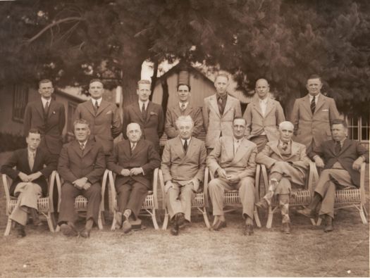 Group of men, seven standing and seven seated, at Royal Canberra Golf Club. Prime Minister Joe Lyons is seated at the centre of the front row. Sir Harry Sheehan is to his left.