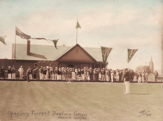 Opening of the Forrest bowling green for the 1931/32 season. Coloured photograph showing a crowd of well dressed people in whites standing in front of the club house and green. There is a woman in the process of bowling.