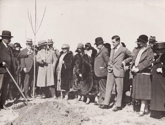 Charles Weston holding a tree and C.S. Daley (hand on hip) with a group of well-dressed men and women looking on