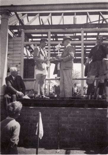 J. Colwell, President of the ACT Hockey Association, presents a cup to the winning captain of a hockey team at Kingston.  Mr. James Brophy is seated at left.
