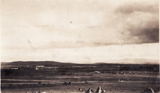 View from below Mt Ainslie near the CSIRO headquarters site on Limestone Avenue looking over mostly bare paddocks (now Reid and Braddon) to old Parliament House.