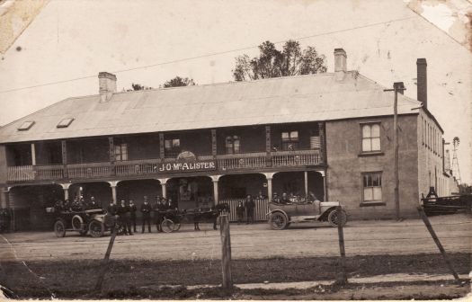 Lake George Hotel, Gibraltar Street, Bungendore. Image shows two cars c1920 and a horse and buggy. About fifteen people are standing or sitting in the vehicles in front of the two story building. The name JO McAlister appears over the entrance.