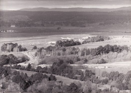 Aerial view of roadworks on Pialligo Avenue associated with the construction of the new Dairy Flat bridge. Canberra Airport is also visible. Two aeroplanes are parked at the terminal.