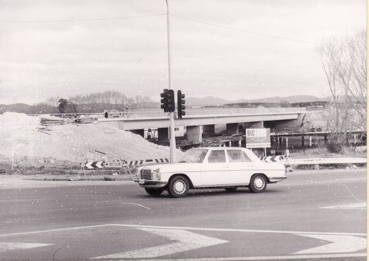 Northern entrance to old Dairy Flat bridge. Shows a Mercedes Benz car driving past traffic lights in the foreground. New bridge under construction, now called the Sylvia Curley Bridge.
