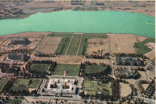 Aerial view of Parliament House from the south showing a recently filled Lake Burley Griffin and the Anzac Park east and west buildings (the portal buildings) under construction.