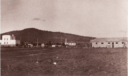 View of office of The Canberra Times, the Canberra Steam Laundry and Coggan's Bakery from near Elourea Street looking south east towards Mt Ainslie. There is a car driving along Mort Street.