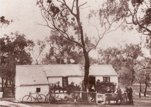 Family portrait in front of the house erected at Duntroon by Frank Dowthwaite. A eucalypt stands in the middle of the garden and two bicycles are leaning against the house and fence. The house is surrounded by woodland. 