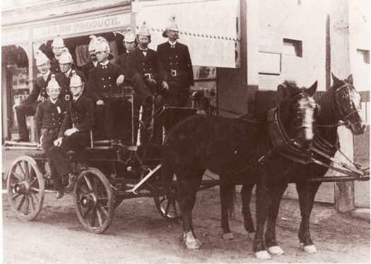 Queanbeyan Fire Brigade. Nine firemen, all dressed in uniform and helmeted, on their horse-drawn fire fighting appliance.