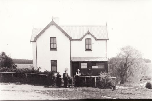 House at Corkhill's farm, demolished in early 1960s to make way for Lake Burley Griffin. Was situated near Yarralumla Bay. Shows a man, woman, boy and girl standing near the fence.