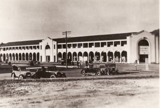 Scene at Civic Centre c1927. View taken from London Circuit and Northbourne Avenue looking north towards the Sydney Building. Snow's store, on the corner of Northbourne Avenue and London Circuit is visible at right. Seven early vintage cars and some pedestrians are visible.