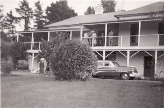 People on the verandah at Lambrigg Homestead. A car is in the driveway at the front of the building.