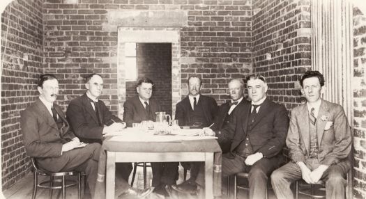 Group of men seated around a table L to R. Rolland, Broinowski, Matthews, Priddle, Col. Owen, Marr, Clarke