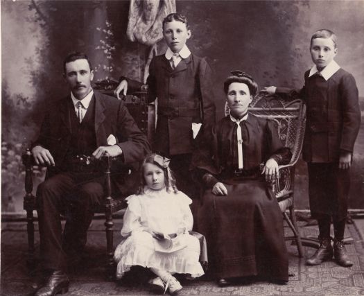 Family portrait, father & mother (seated), two sons standing and daughter sitting on the floor between her parents.