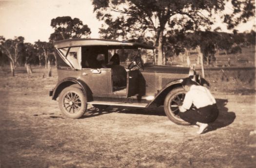 A man checking the front tyre of a vintage car.