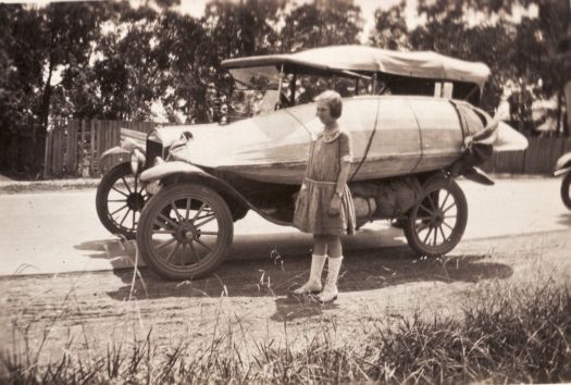 Canoe tied to the side of a Model T Ford. Unidentified girl is standing next to the car.