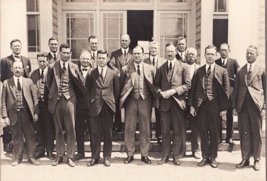 A group of seventeen men, personnel from the Home Affairs, standing in front of the offices at Acton. CS Daley is in the front row.