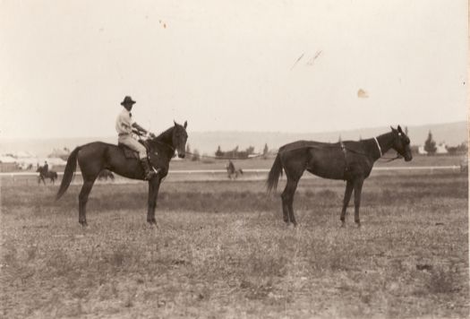 Unidentified man riding a horse, trailing another horse.