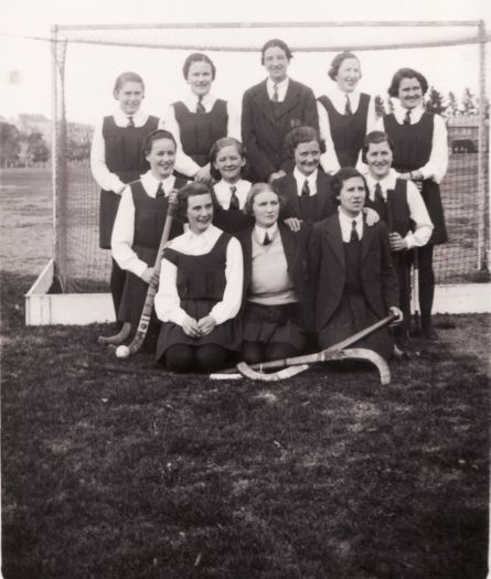 Twelve schoolgirls from a hockey team posed in front of goal.