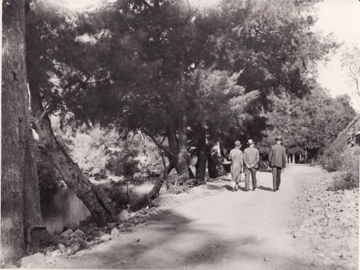Rear view of two men and a woman (circa 1920s) walking along a path next to a river.