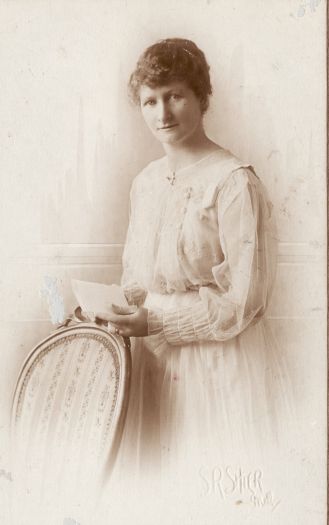 Portrait of an unidentified woman standing behind a chair.