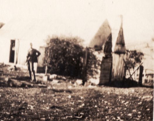 Blurred image of a man standing in front of slab house with stone or brick chimney - unknown site