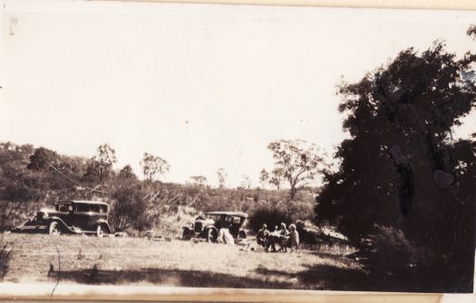 Camp on Cotter River showing two cars and a group of people sitting at a table probably having a picnic