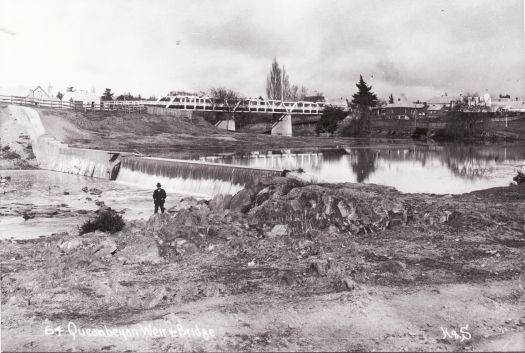 Man standing in front of the Queanbeyan weir with the Queen's Bridge in the background