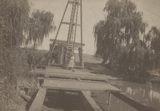 Two level bridge after flood of 1914. Planks are missing from the bridge. A crane is in the background and an unknown woman is standing in front of the crane.