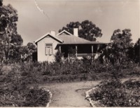 Acton cottage type, front view. A garden is in the foreground with a path lined by small stones. Home is built approximately 2 metres off the ground.