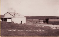 Shows the brickworks' buildings in the foreground. In the distance is a bare hill with a small building on the crest.
