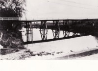 First Commonwealth Avenue bridge over the Molonglo River. The bridge is wooden with white railings. Foreground shows part of a low level bridge.