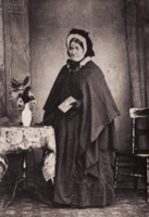 Mrs. Susan Blundell (1796-1892), wife of Joseph Blundell, a member of the pioneering Blundell family. Mrs. Blundell is standing near a small table with a vase of flowers on it.